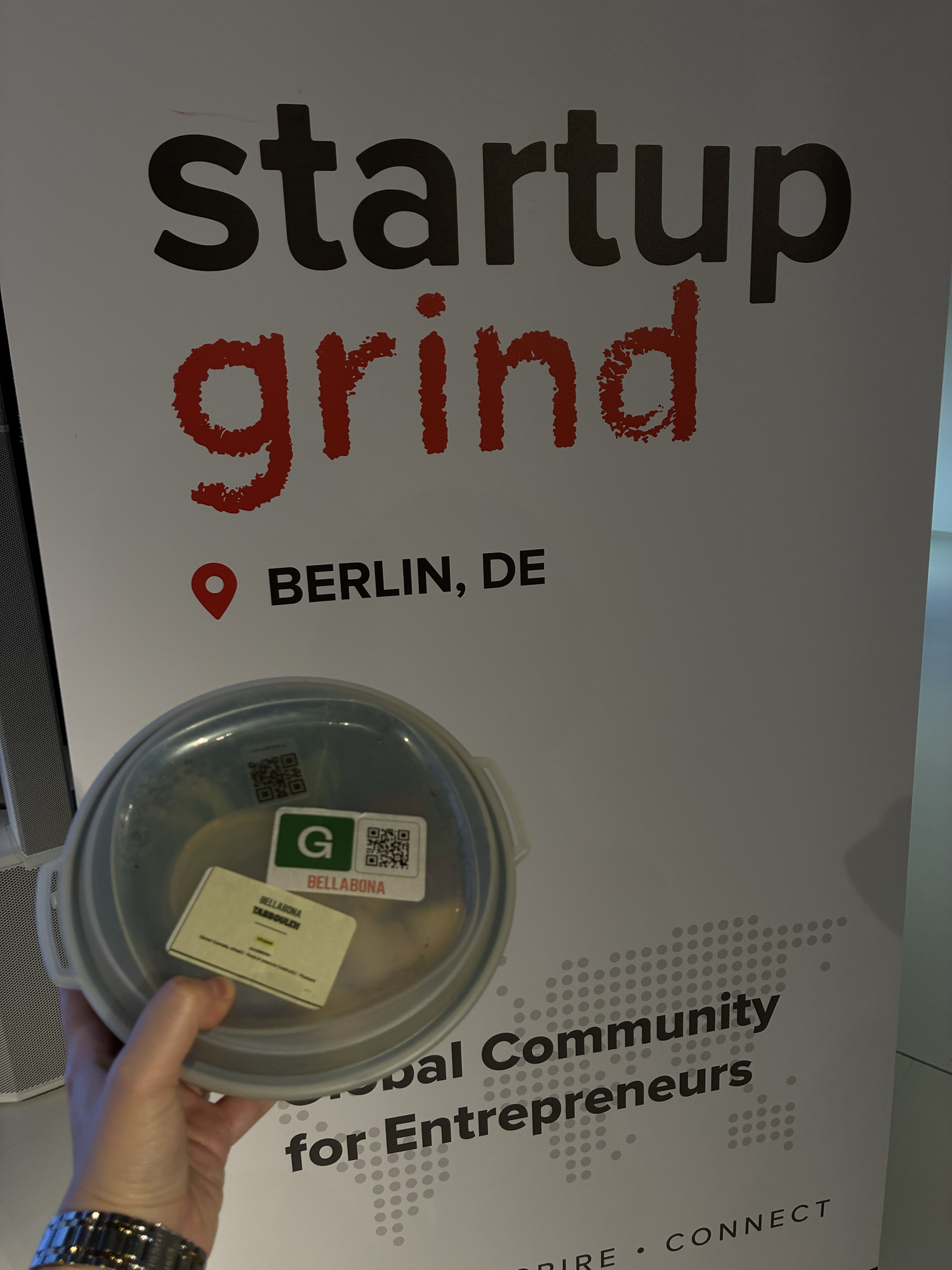 A labelled Bella&Bona lunch box held in front of the Startup Grind banner