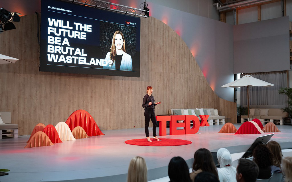A speaker on the red carpet in front of the slide “Will the future be a brutal wasteland?”