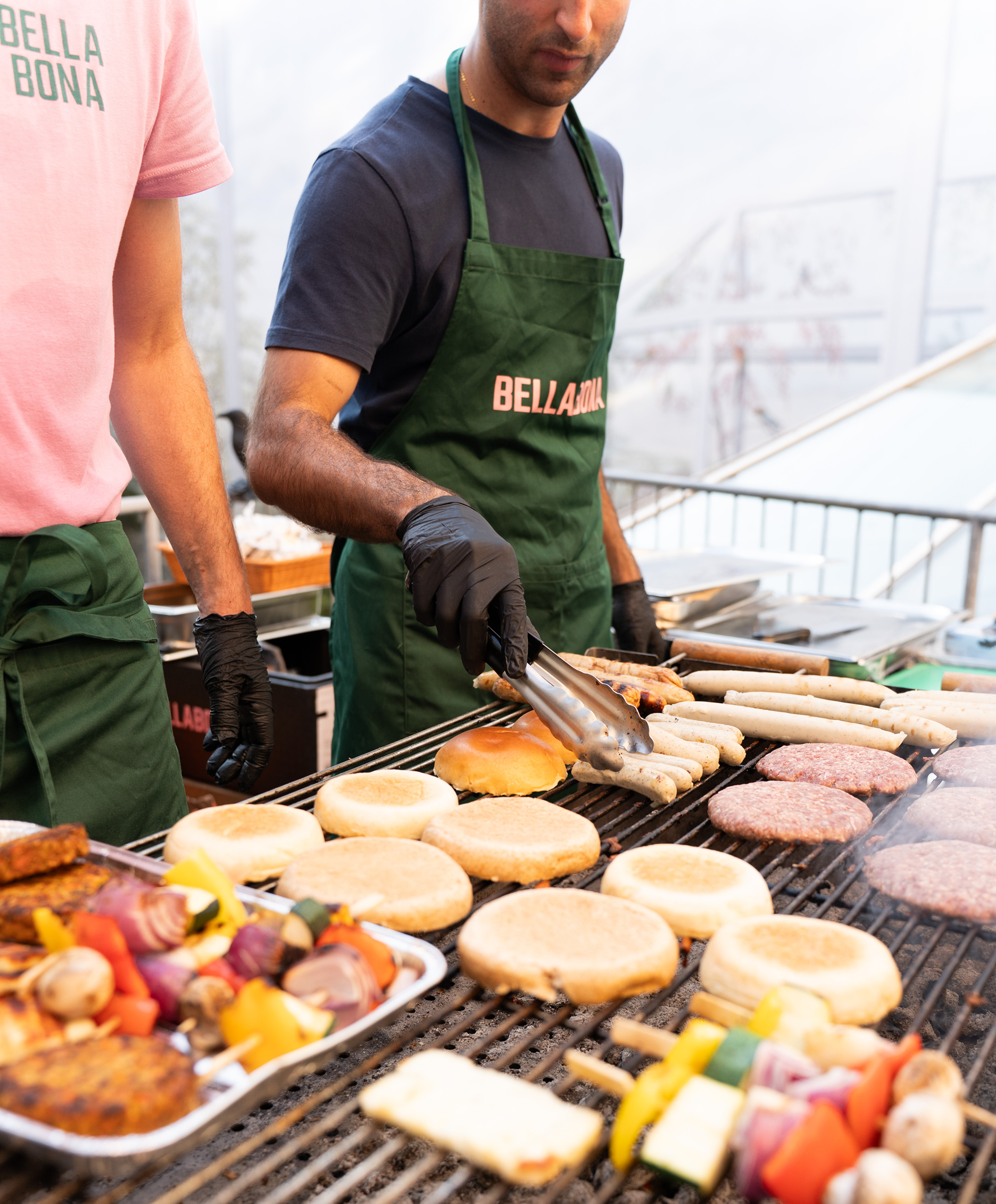 A Bella&Bona chef grilling sausages and burgers at an event