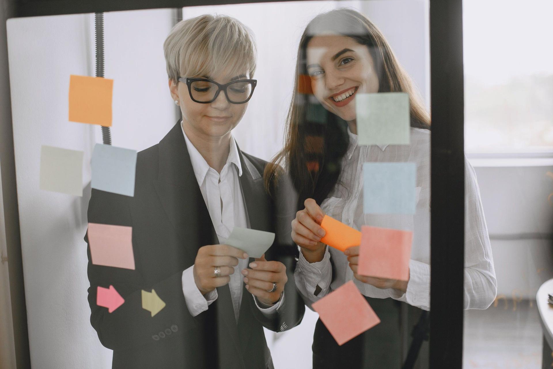 Two colleagues planning with colourful sticky notes on a glass wall