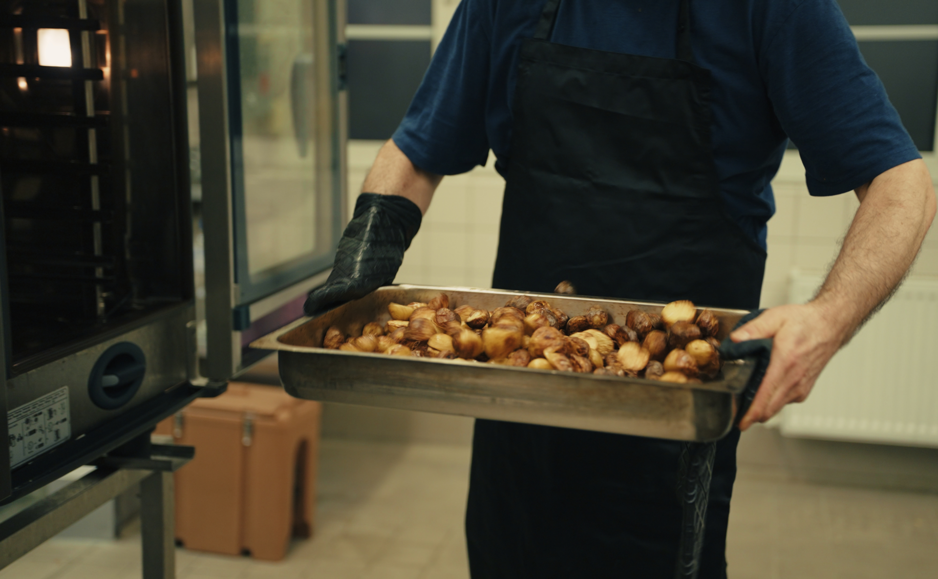 Koch trägt ein Blech mit frisch gebackenen Brötchen aus dem Ofen in der Bella&Bona Küche