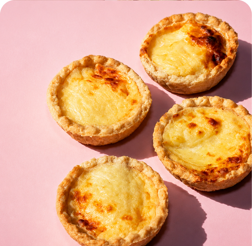 Four baked egg tarts on a pink background