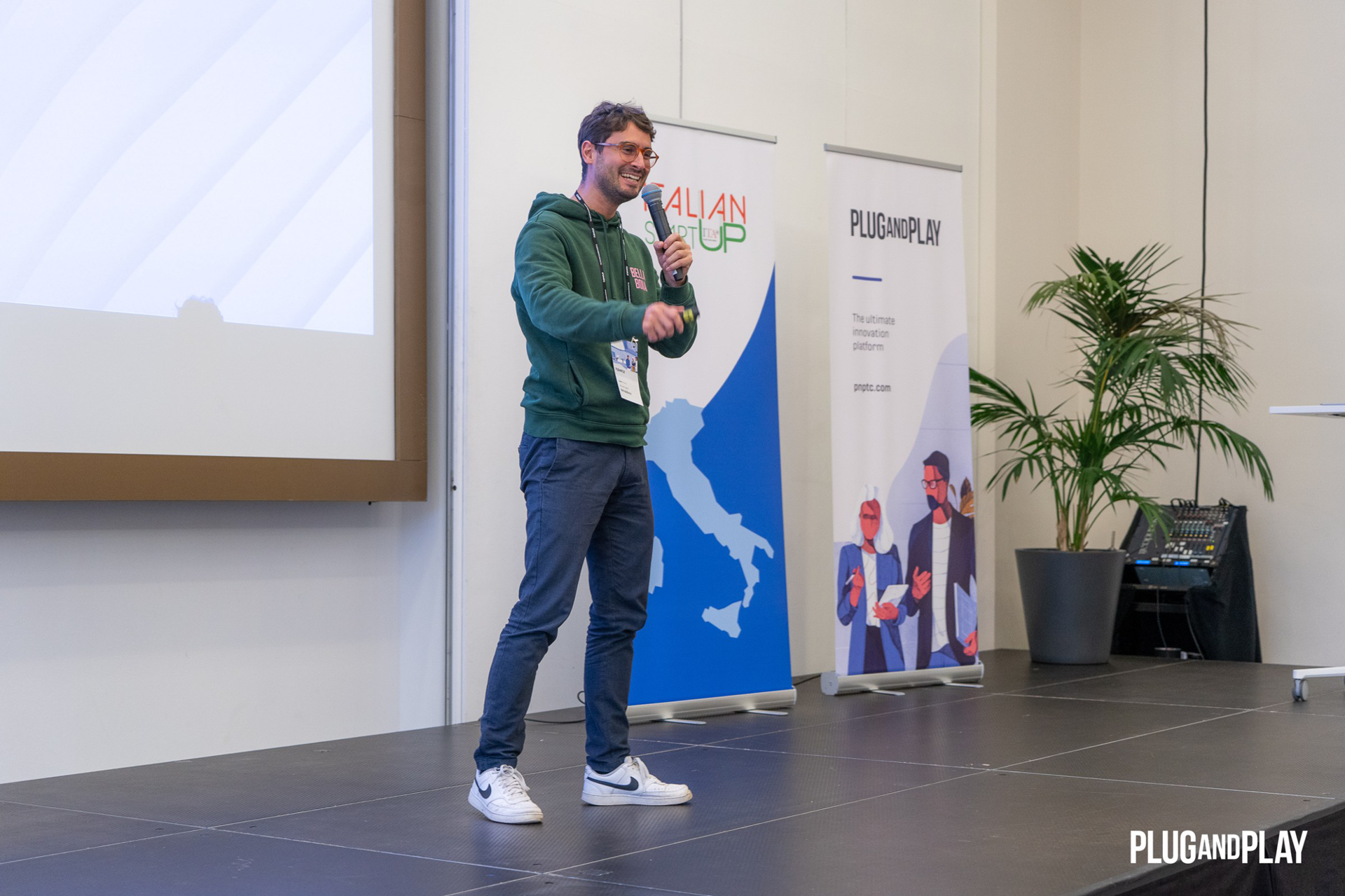 Niccolò on stage with the microphone, next to the Italian Startup banner