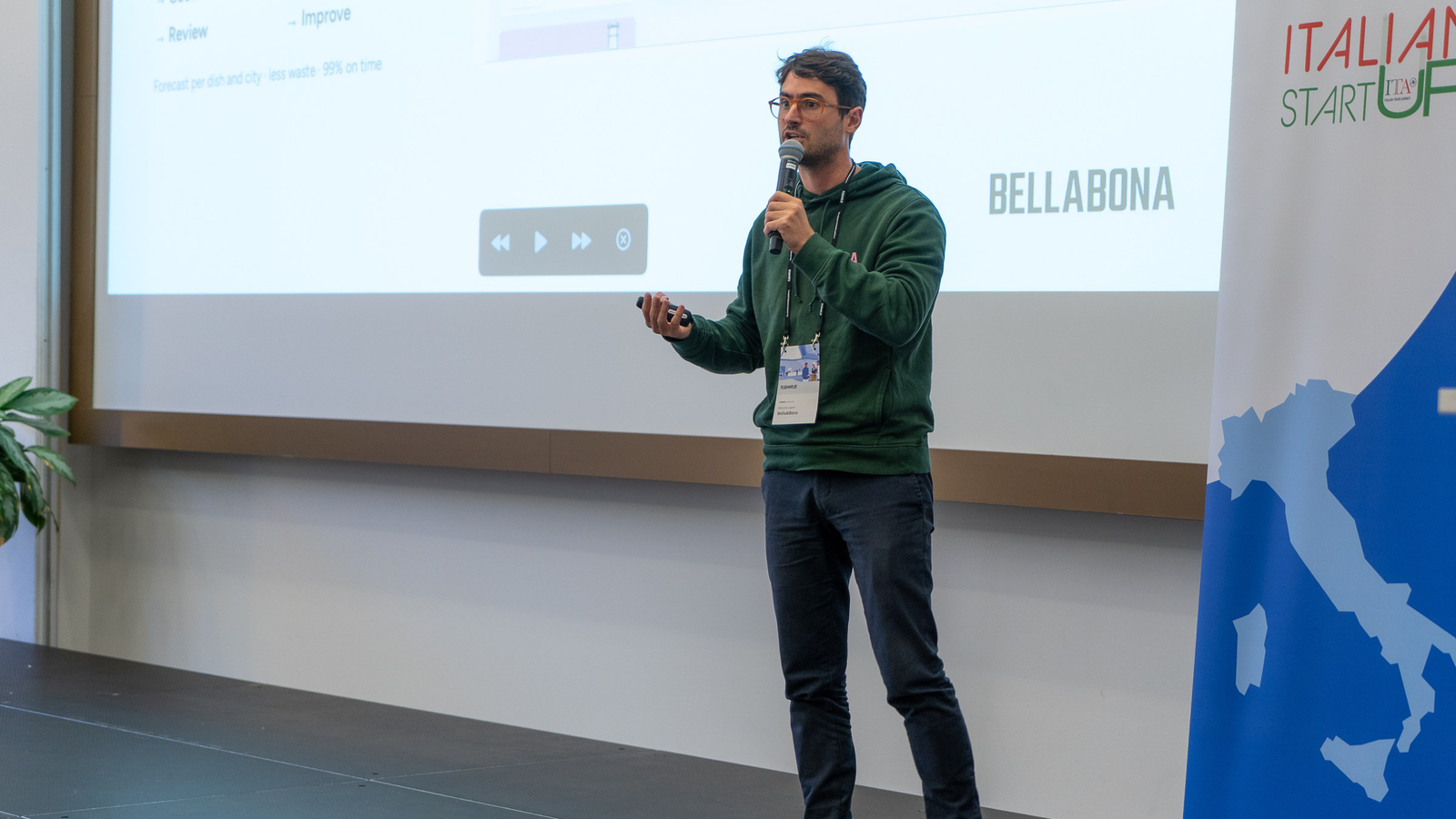Niccolò Lapini hält die Keynote, hinter ihm das Bella&Bona-Logo auf der Leinwand
